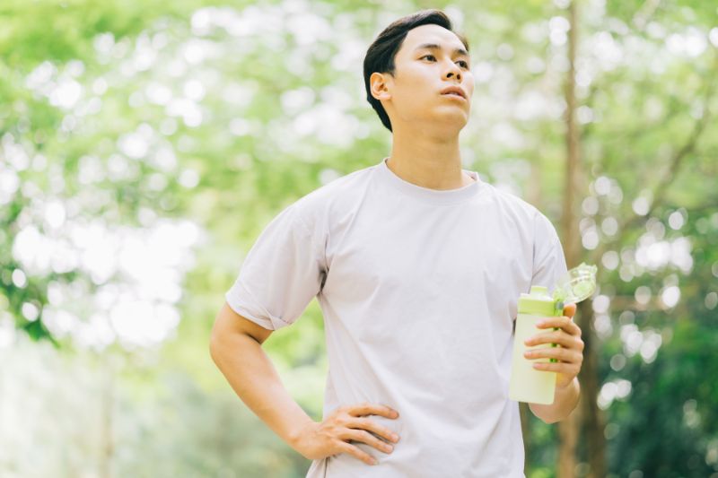 森の中で水筒を片手に持ったTシャツ姿の男性