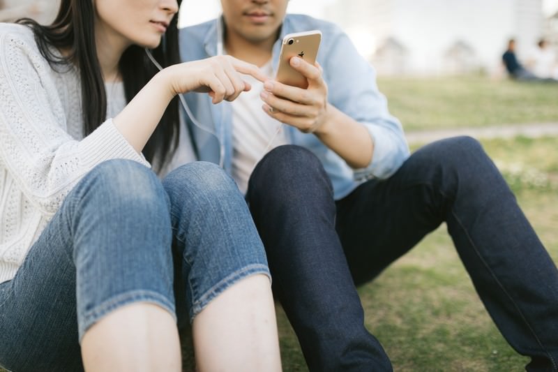 芝生に座りスマホを見ながら語り合う男女