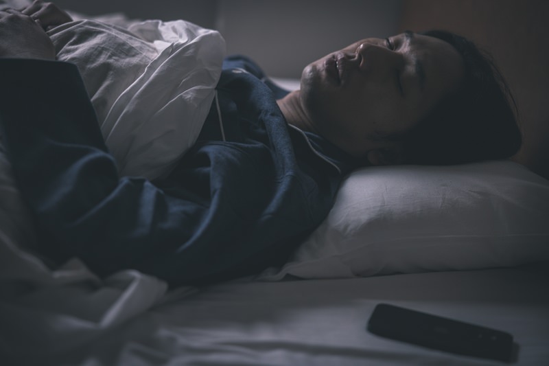 スマートフォンを枕元に置いてベッドで眠る男性